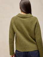 A woman viewed from the back wearing Shepherd Collar Cardi – Mid Chartreuse with a ribbed mock neck and raglan sleeves, paired with dark blue jeans against a neutral beige background.