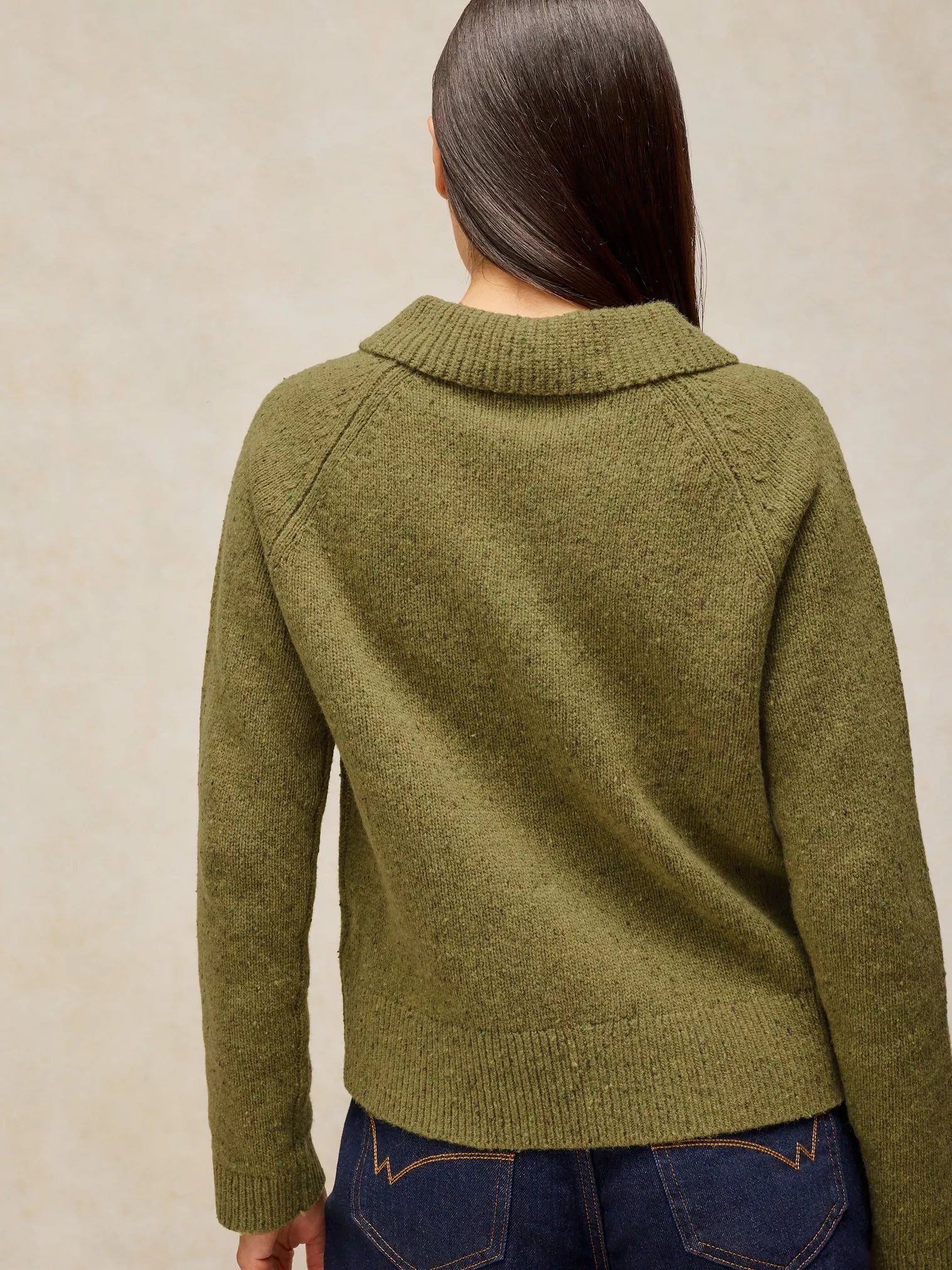 A woman viewed from the back wearing Shepherd Collar Cardi – Mid Chartreuse with a ribbed mock neck and raglan sleeves, paired with dark blue jeans against a neutral beige background.