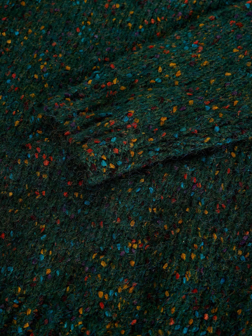 A close-up of a dark green textured fabric with a multicolor speckled pattern of small orange, blue, red, and yellow flecks.
