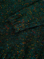 A close-up of a dark green textured fabric with a multicolor speckled pattern of small orange, blue, red, and yellow flecks.