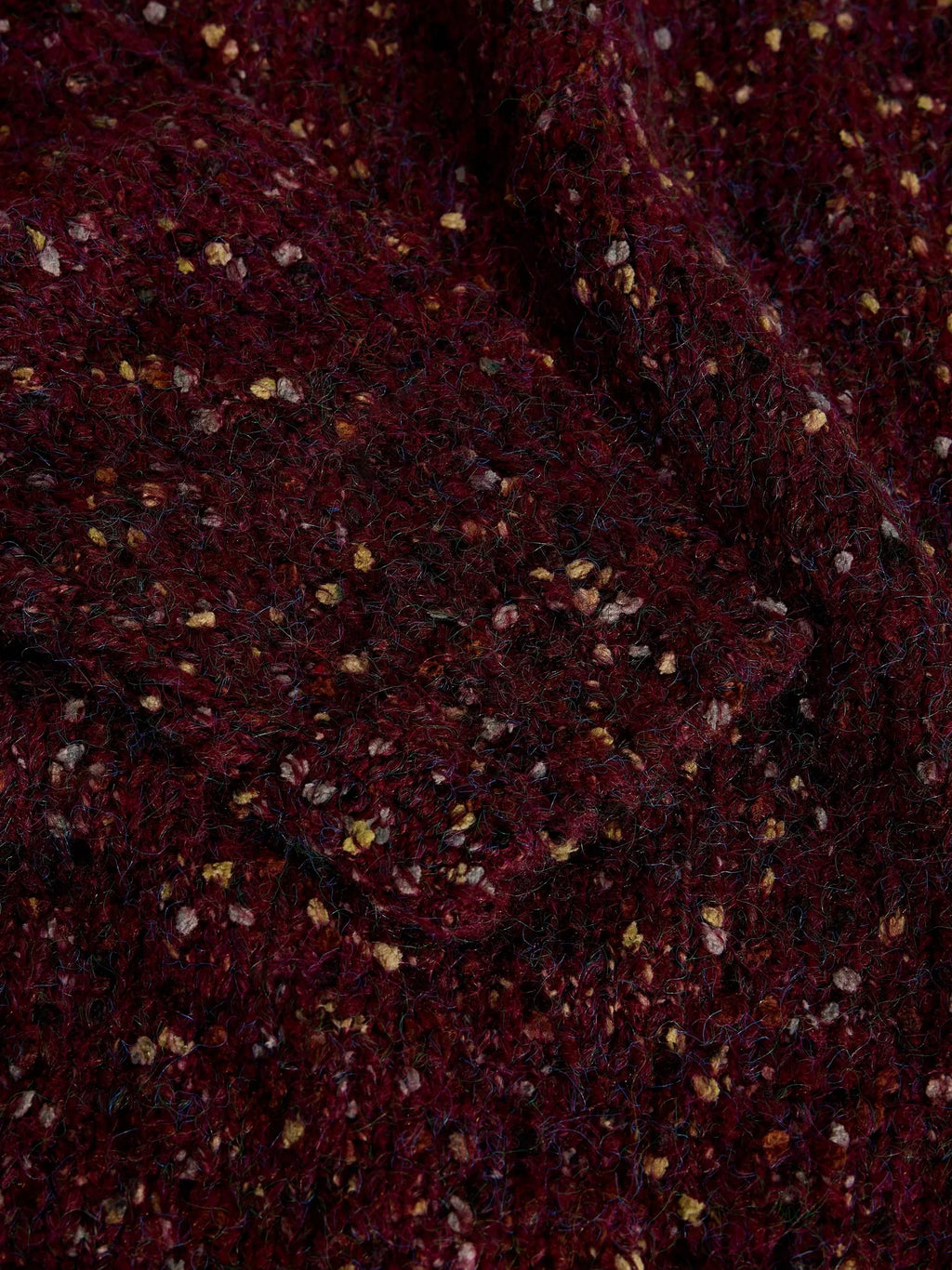 A close-up of a dark burgundy or maroon textured fabric with small scattered metallic gold and silver flecks.