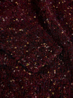 A close-up of a dark burgundy or maroon textured fabric with small scattered metallic gold and silver flecks.
