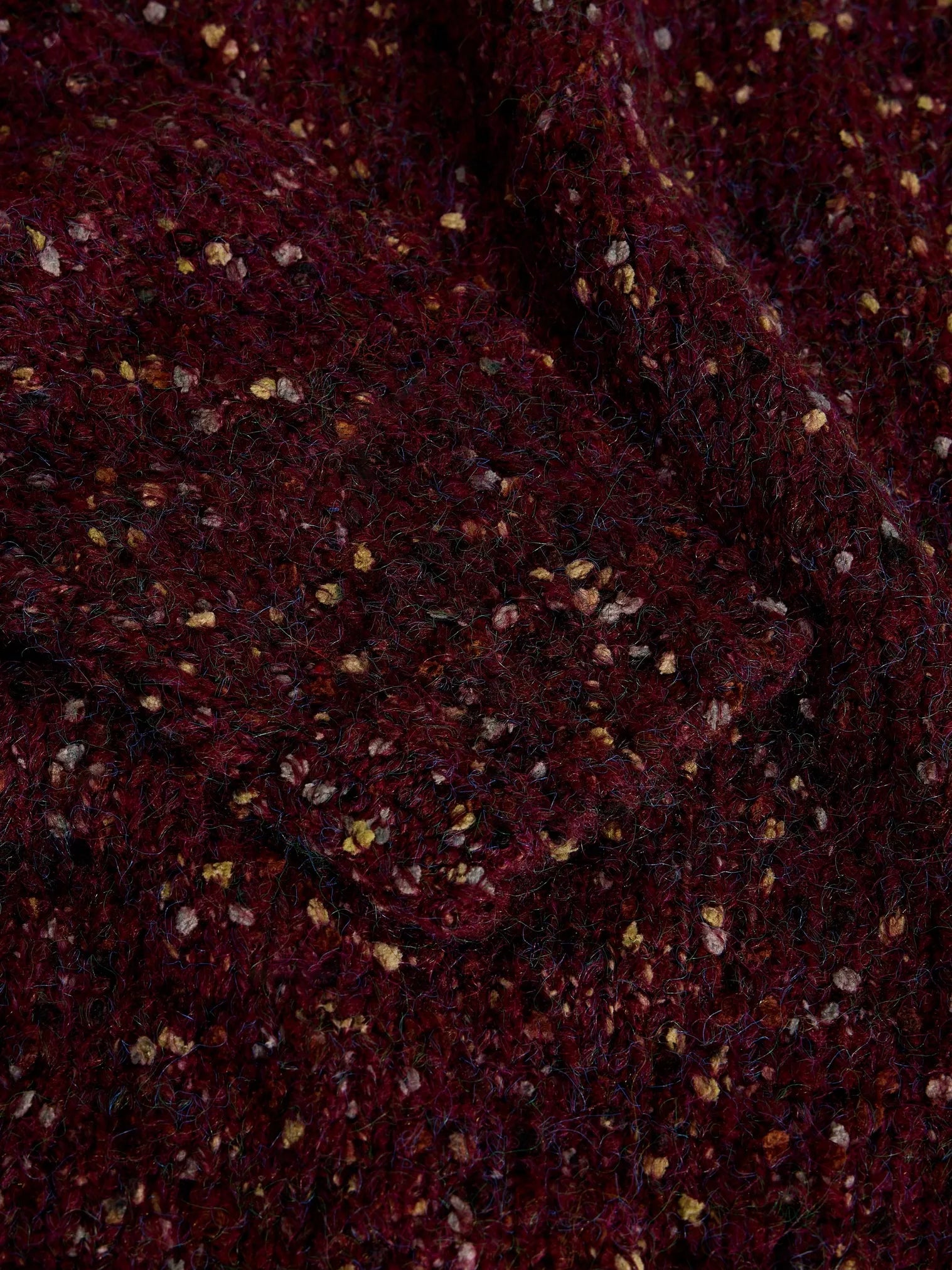 A close-up of a dark burgundy or maroon textured fabric with small scattered metallic gold and silver flecks.