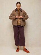 Person wearing a plaid jacket, brown shirt, TIA brown WIDE LEG CROP JEAN and orange shoes against a beige background
