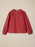 LANA dusty PINk BABY CORD TOP with gathered puff sleeves and a button-up front, laid flat against a textured beige background.