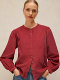 A woman wearing a long-sleeve button-front LANA dusty PINk BABY CORD TOP , paired with blue jeans, against a neutral beige background.