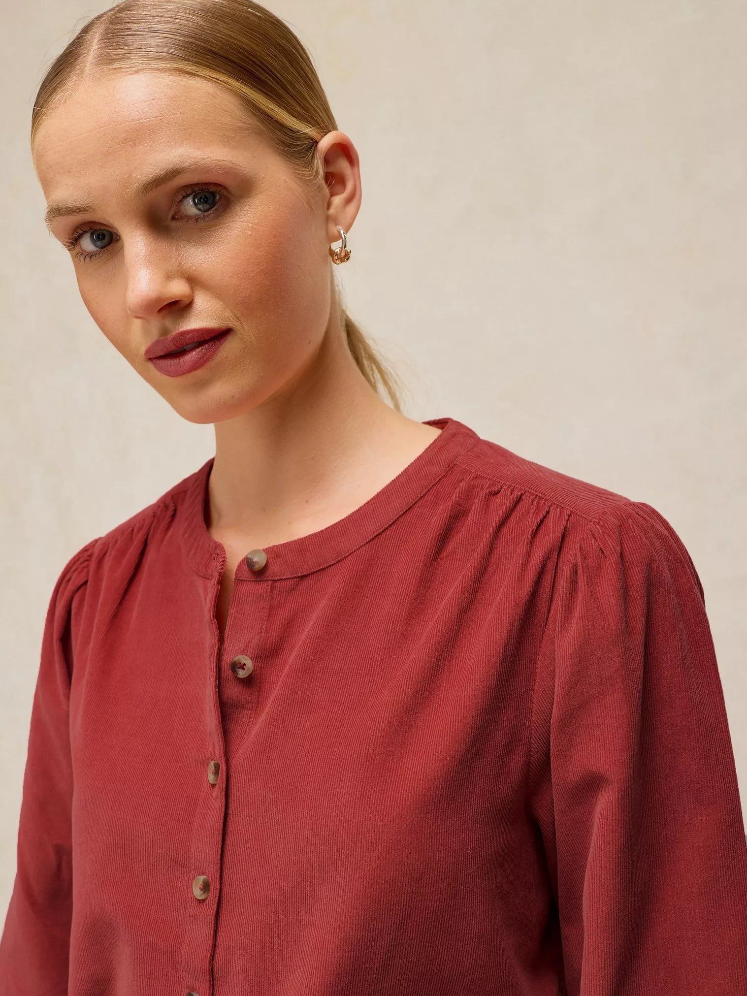 A close-up shot of a woman wearing a LANA dusty PINk BABY CORD TOP  with a buttoned round neckline, set against a neutral beige background.