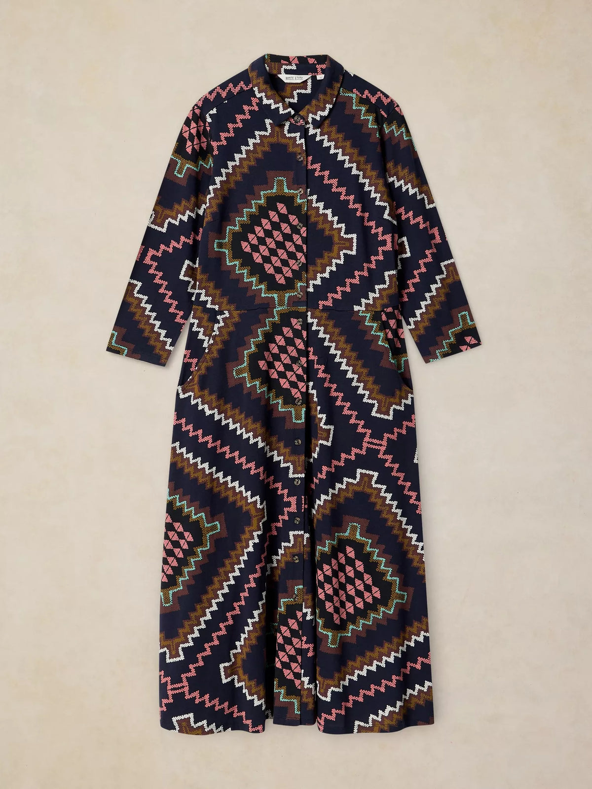 Rua Jersey Dress in Navy Multi with a geometric Southwestern pattern in navy, pink, brown, white, and green, laid flat against a light beige background.
