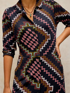 A close-up of a model wearing a Rua Jersey Dress in Navy Multiwith a dark navy base and a colorful geometric tribal pattern in pink, brown, white, and green.