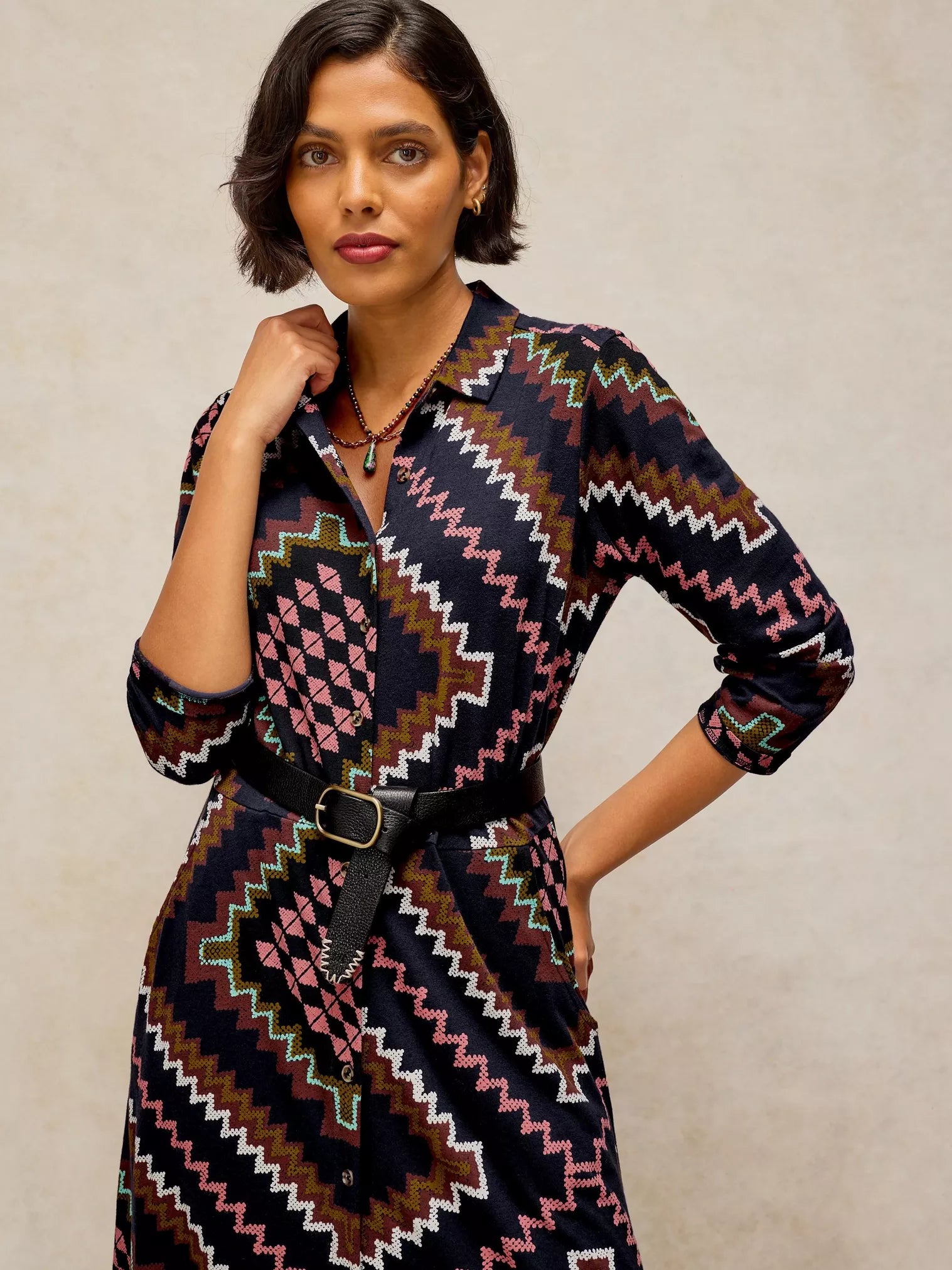 A woman modeling Rua Jersey Dress in Navy Multi with a colorful geometric pattern in pink, brown, green, and white on a dark navy base, styled with a black belt.