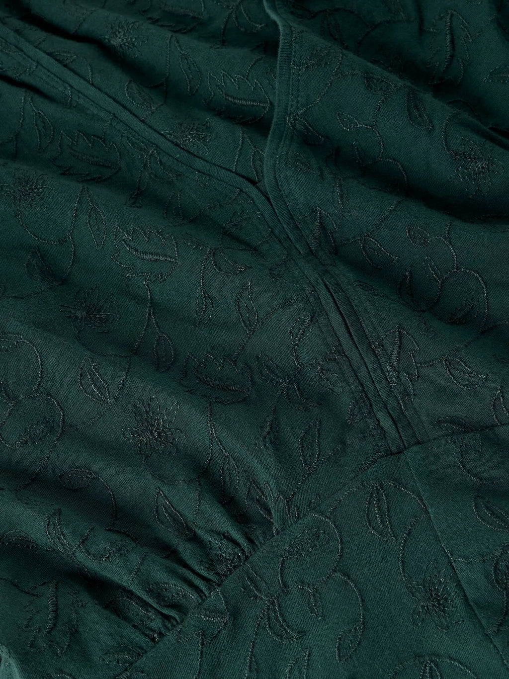 Close-up of a dark forest green fabric with a subtle tonal floral jacquard pattern and gathered seams.
