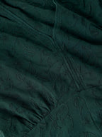Close-up of a dark forest green fabric with a subtle tonal floral jacquard pattern and gathered seams.