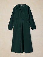 A dark forest green long-sleeve midi dress with a V-neckline and gathered waist details, displayed flat against a textured beige background.