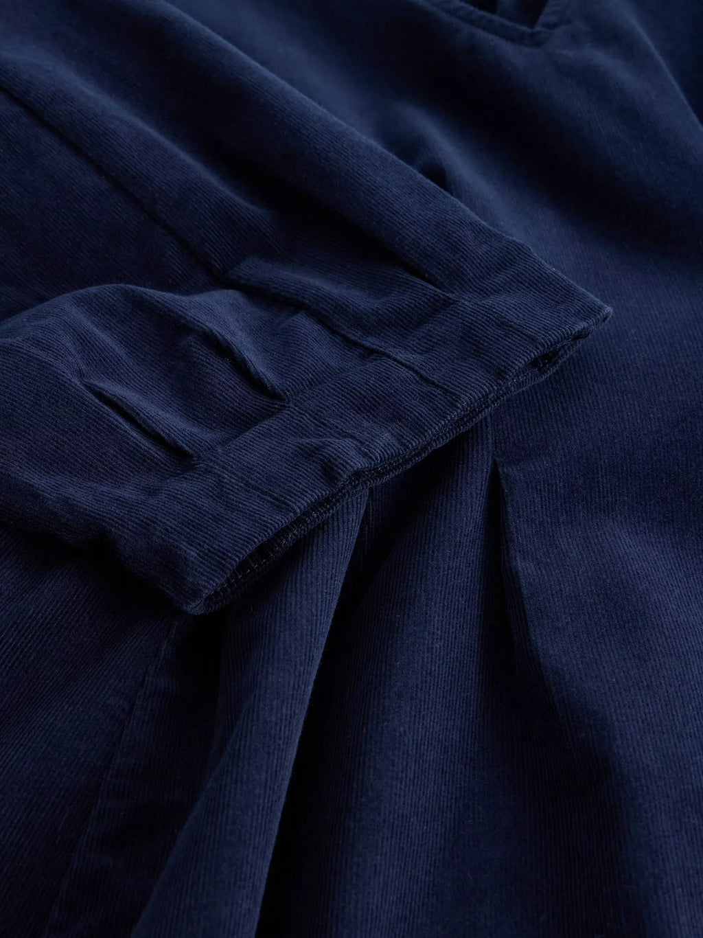 Close-up of dark navy blue corduroy fabric with visible ribbed texture and folded pleats.