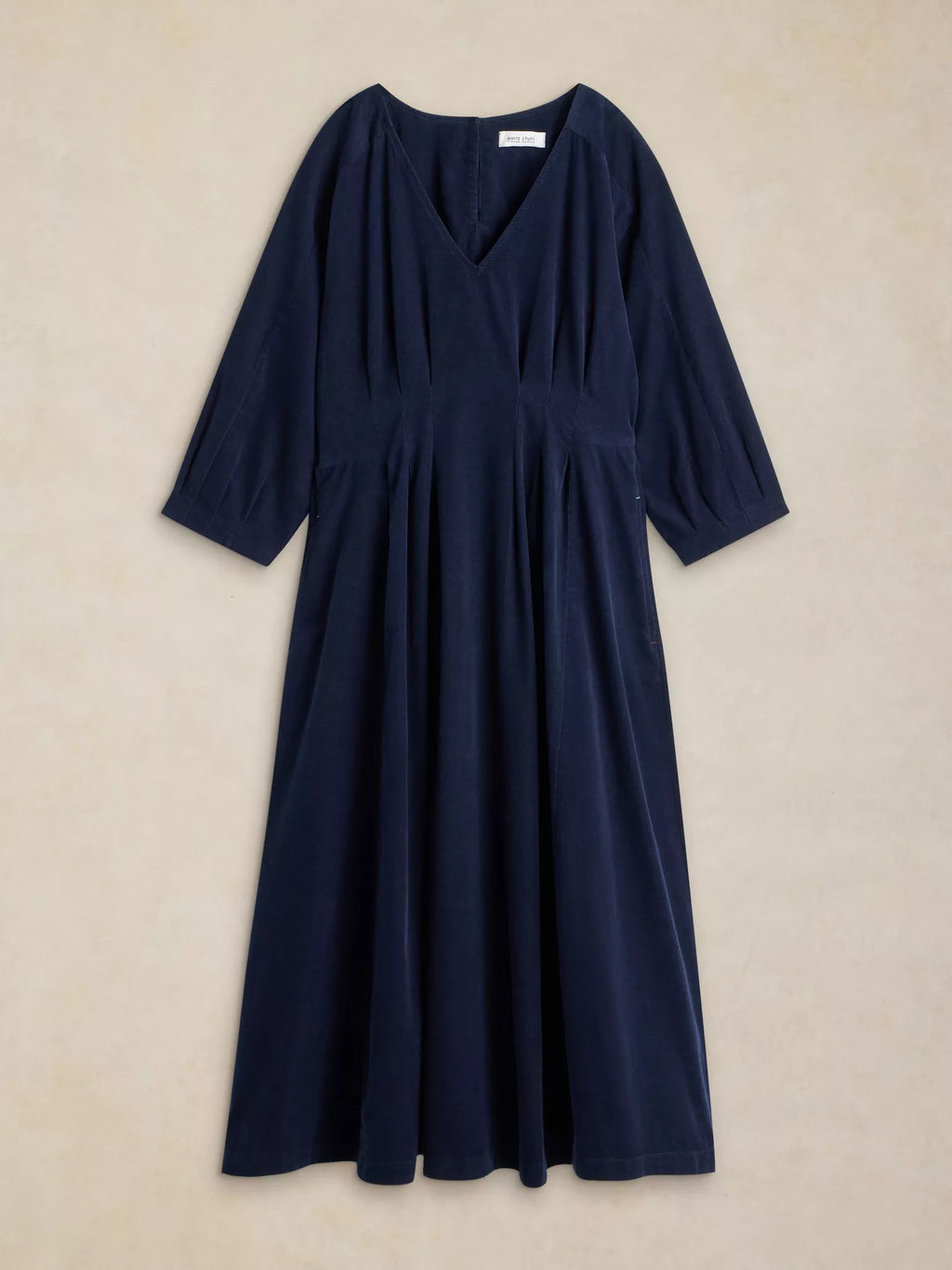 A dark navy blue midi dress with three-quarter sleeves, a V-neckline, and a gathered empire waist, displayed flat against a textured beige background.