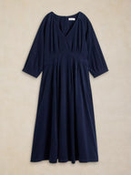 A dark navy blue midi dress with three-quarter sleeves, a V-neckline, and a gathered empire waist, displayed flat against a textured beige background.