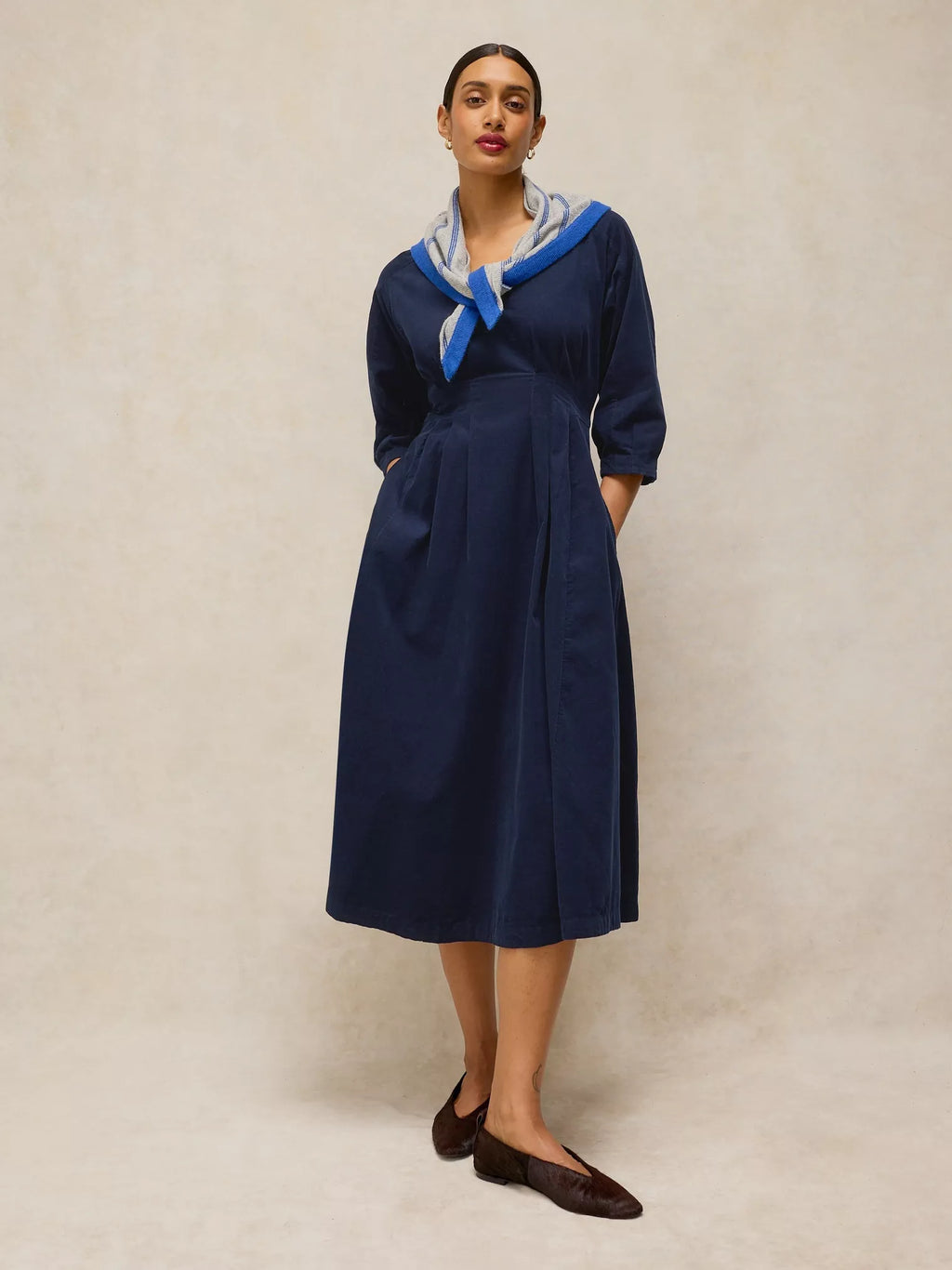 Woman wearing a navy blue dress with a blue scarf against a beige background