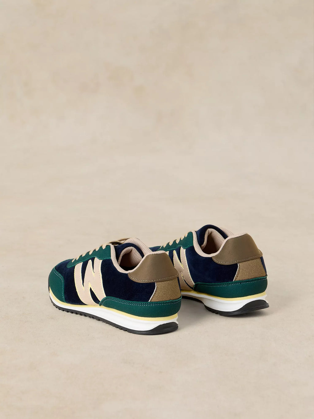 A pair of A Lucy Trainer sneaker in Blue multi in navy blue suede and green mesh with beige accents, shown from a rear three-quarter view on a neutral beige background.