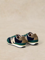 A pair of A Lucy Trainer sneaker in Blue multi in navy blue suede and green mesh with beige accents, shown from a rear three-quarter view on a neutral beige background.