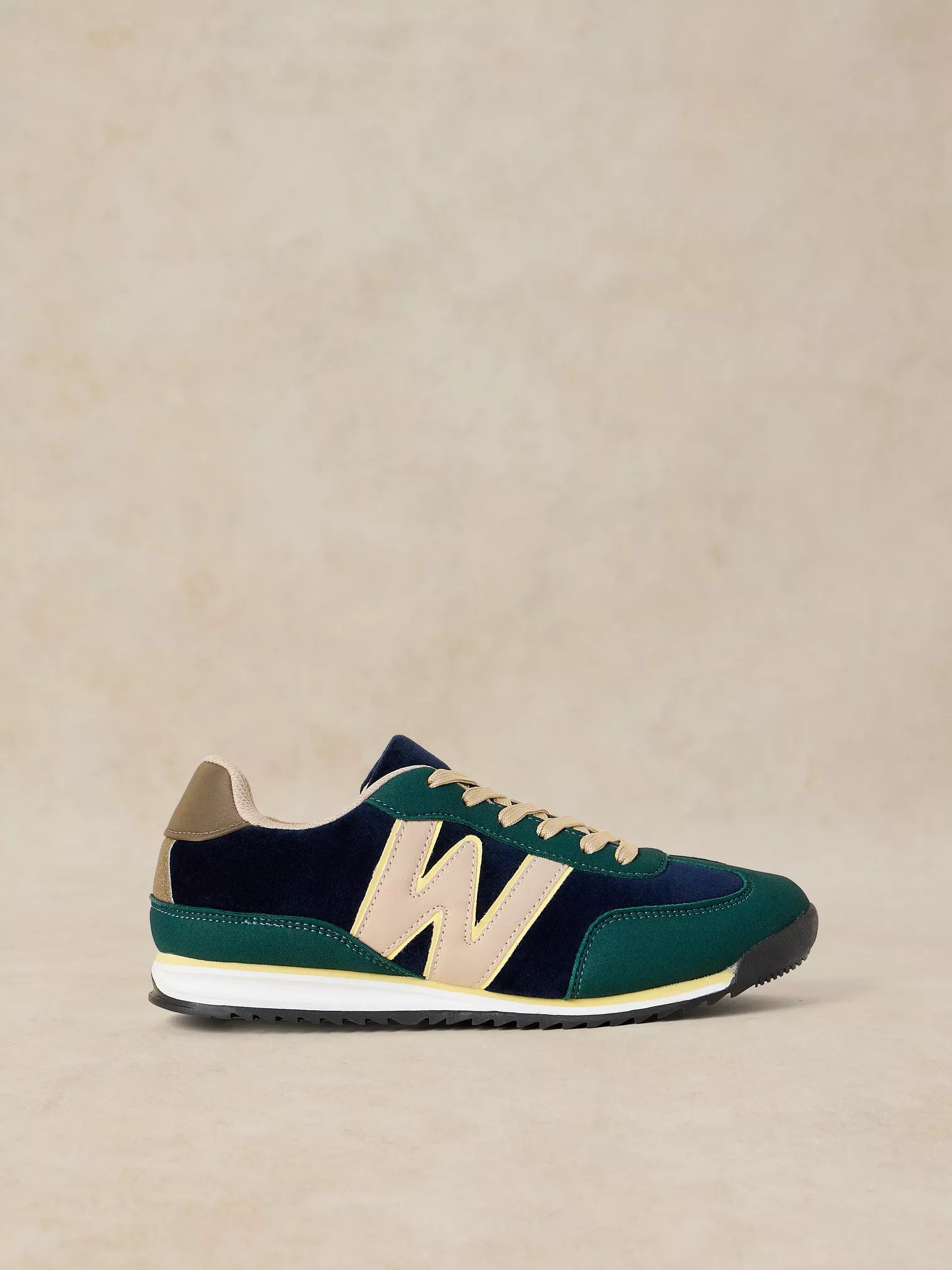 A Lucy Trainer sneaker in Blue multi in dark green and navy suede with beige accents, including the iconic 'N' logo, laces, and heel tab, set against a neutral beige background.