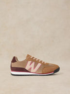 A Lucy Trainer sneaker in Natural multi and corduroy with a large light pink 'W' logo, burgundy heel tab, and a white midsole with a thin pink stripe, set against a neutral beige background.