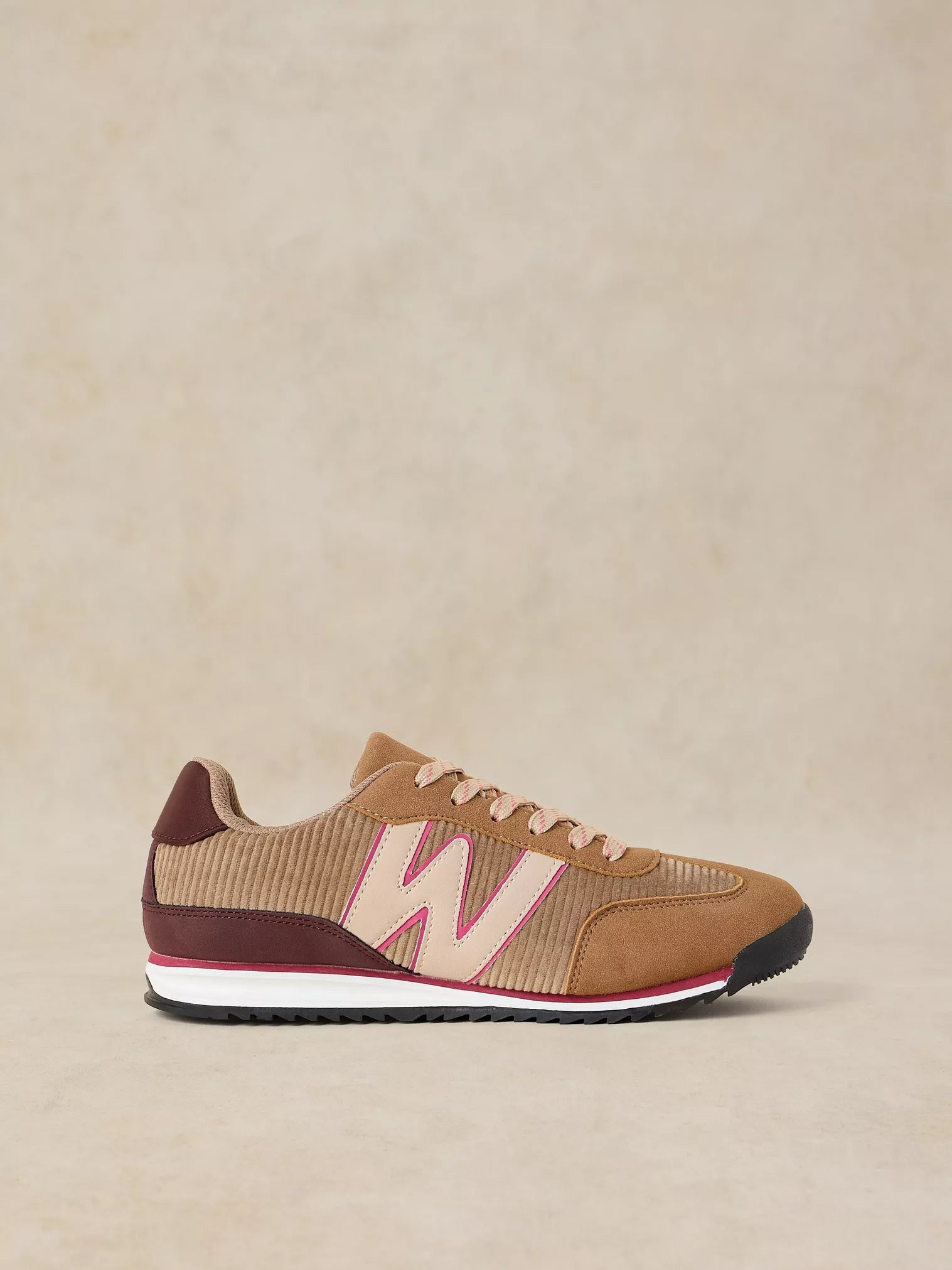 A Lucy Trainer sneaker in Natural multi and corduroy with a large light pink 'W' logo, burgundy heel tab, and a white midsole with a thin pink stripe, set against a neutral beige background.