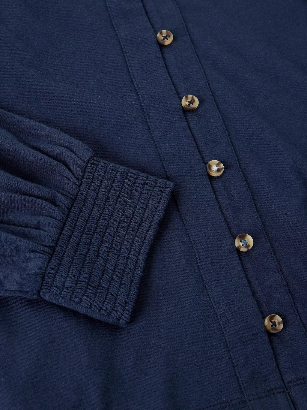 Close-up of a navy blue long-sleeve button-up shirt showing the smocked elastic cuff and metallic buttons.
