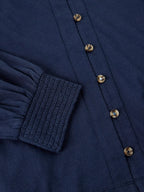 Close-up of a navy blue long-sleeve button-up shirt showing the smocked elastic cuff and metallic buttons.