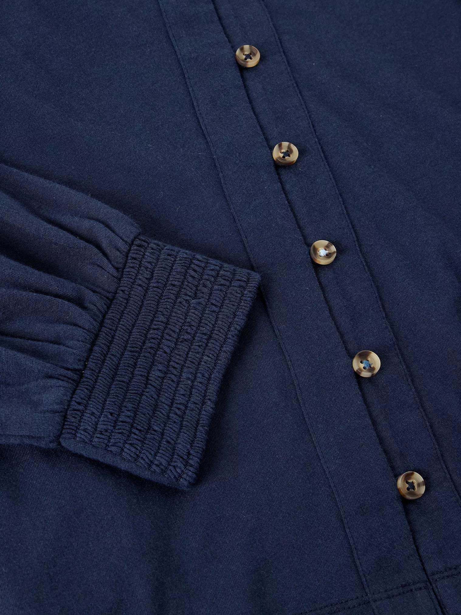 Close-up of a navy blue long-sleeve button-up shirt showing the smocked elastic cuff and metallic buttons.