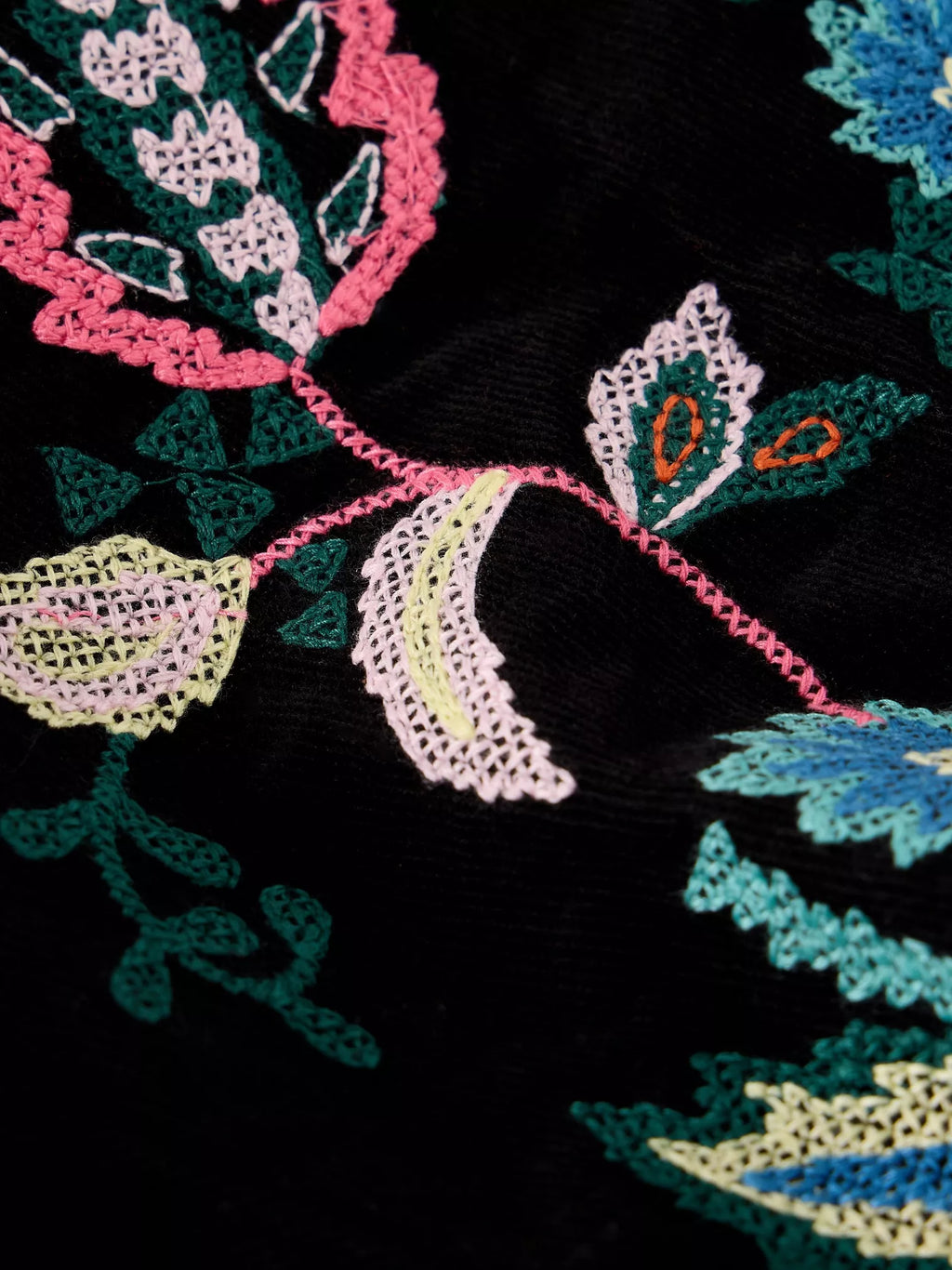 Close-up of a black embroidered textile featuring floral and leaf motifs in pink, teal, light green, pale yellow, and small orange accents.