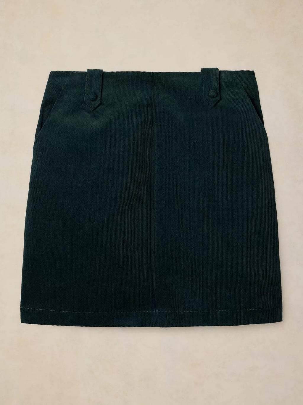 A dark forest green mini skirt with belt loops and side pockets, laid flat on a light beige textured background.
