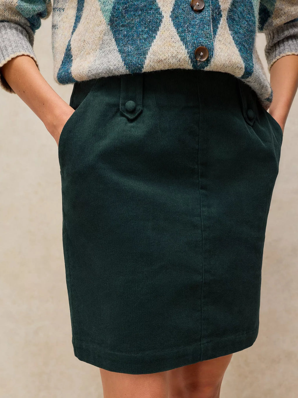 A dark forest green skirt with a button closure and side pockets, styled with a blue, beige, and gray argyle cardigan sweater.