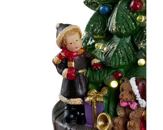 Christmas-themed figurine with a child and teddy bear near a decorated tree on a white background
