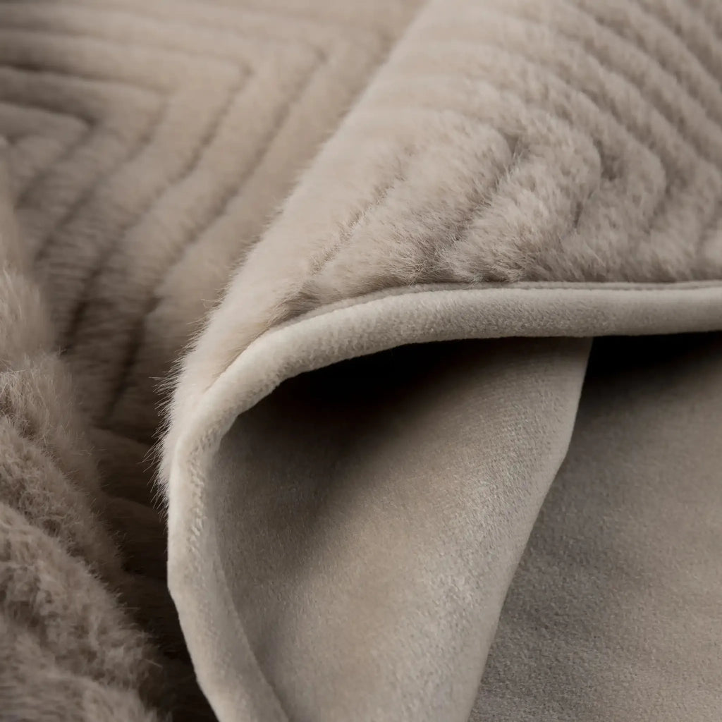 Close-up of a soft, plush throw blanket in a warm light beige or Ellis Throw in Mink - showing quilted texture on one side and a smoother fabric underside on the other.