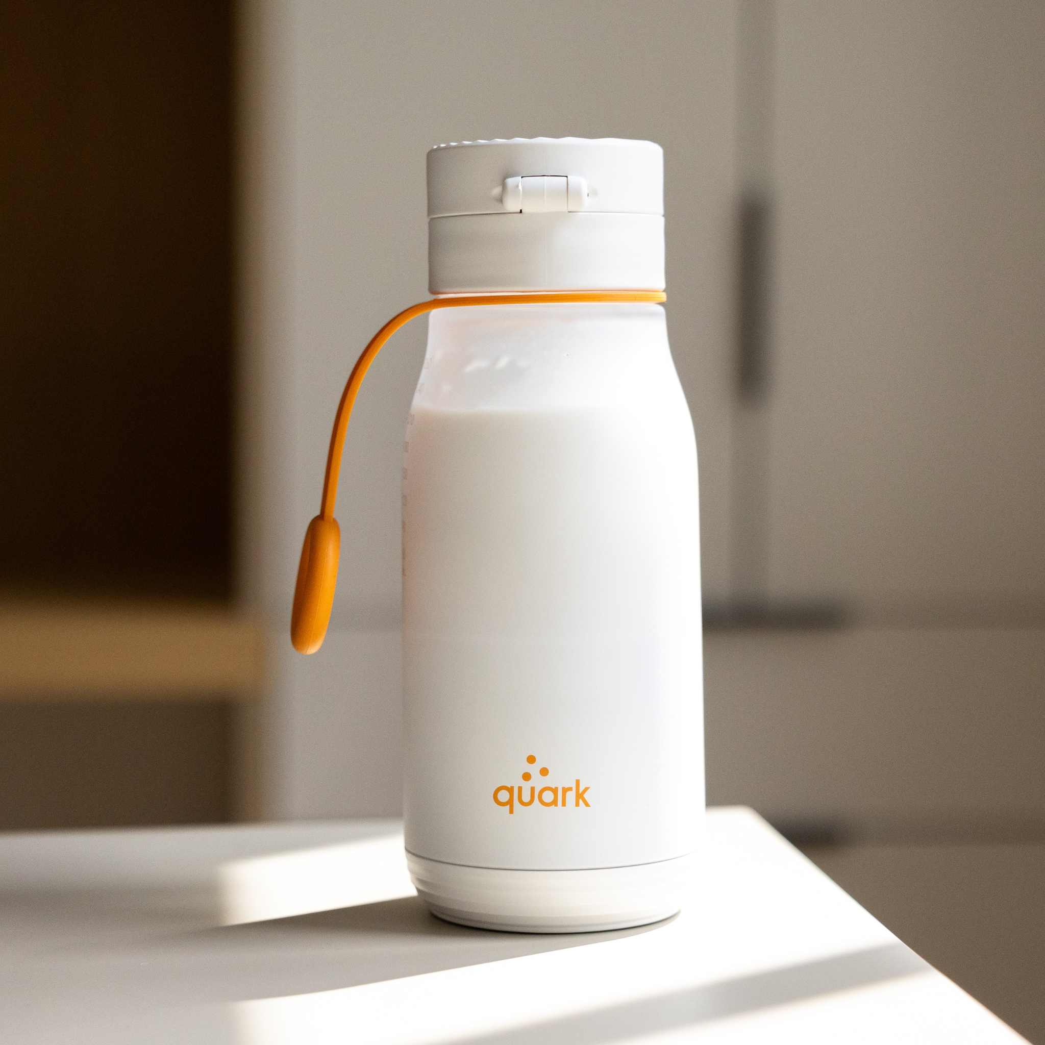 White water bottle with orange accent on a white surface, featuring the 'quark' brand.