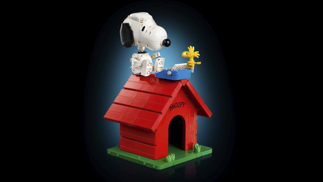 A Snoopy and Woodstock dog house figurine featuring Snoopy sitting on top of a red dog house with a green base, set against a dark blue gradient background.