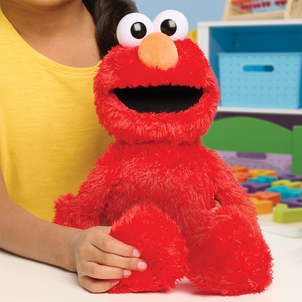 Tickle Me Elmo and a Girl wearing a yellow top in a bedroom background