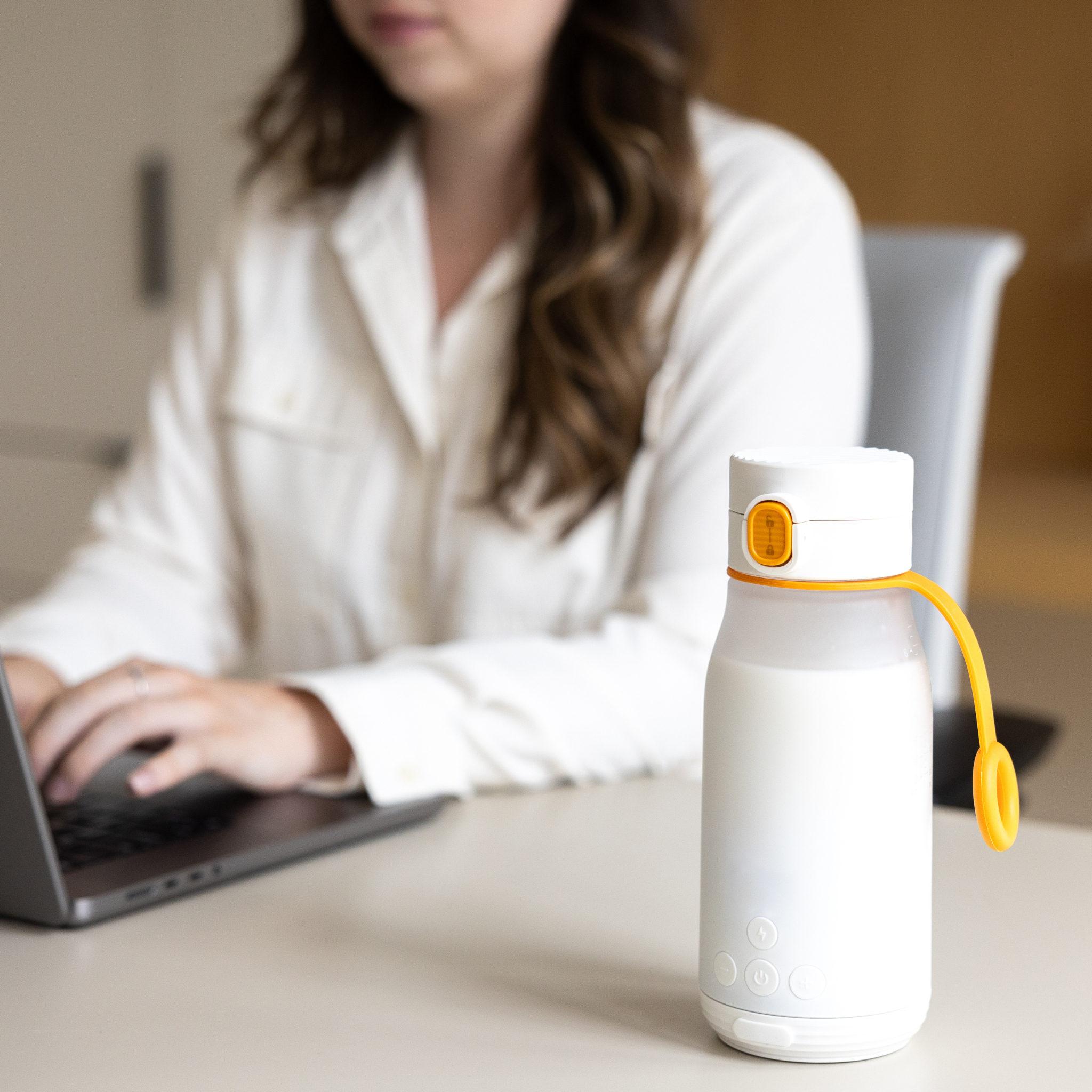 Person using a laptop with a white water bottle with a yellow cap on a desk