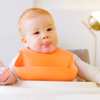 Baby wearing an orange bib sitting in a high chair.