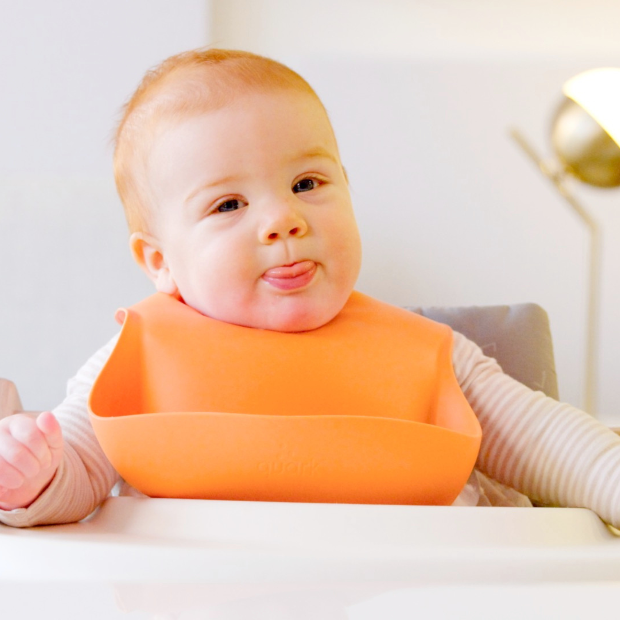 Baby wearing an orange bib sitting in a high chair.