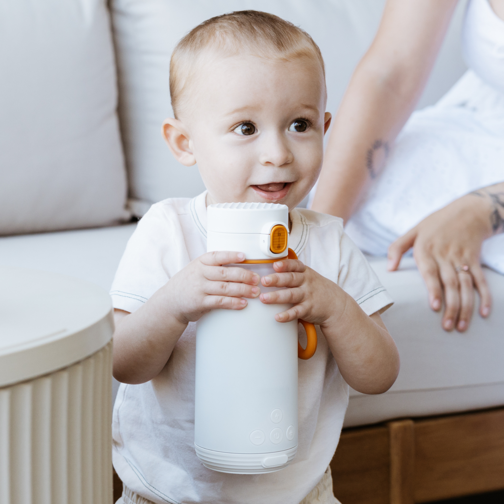 Child holding a white cup with an orange handle indoors