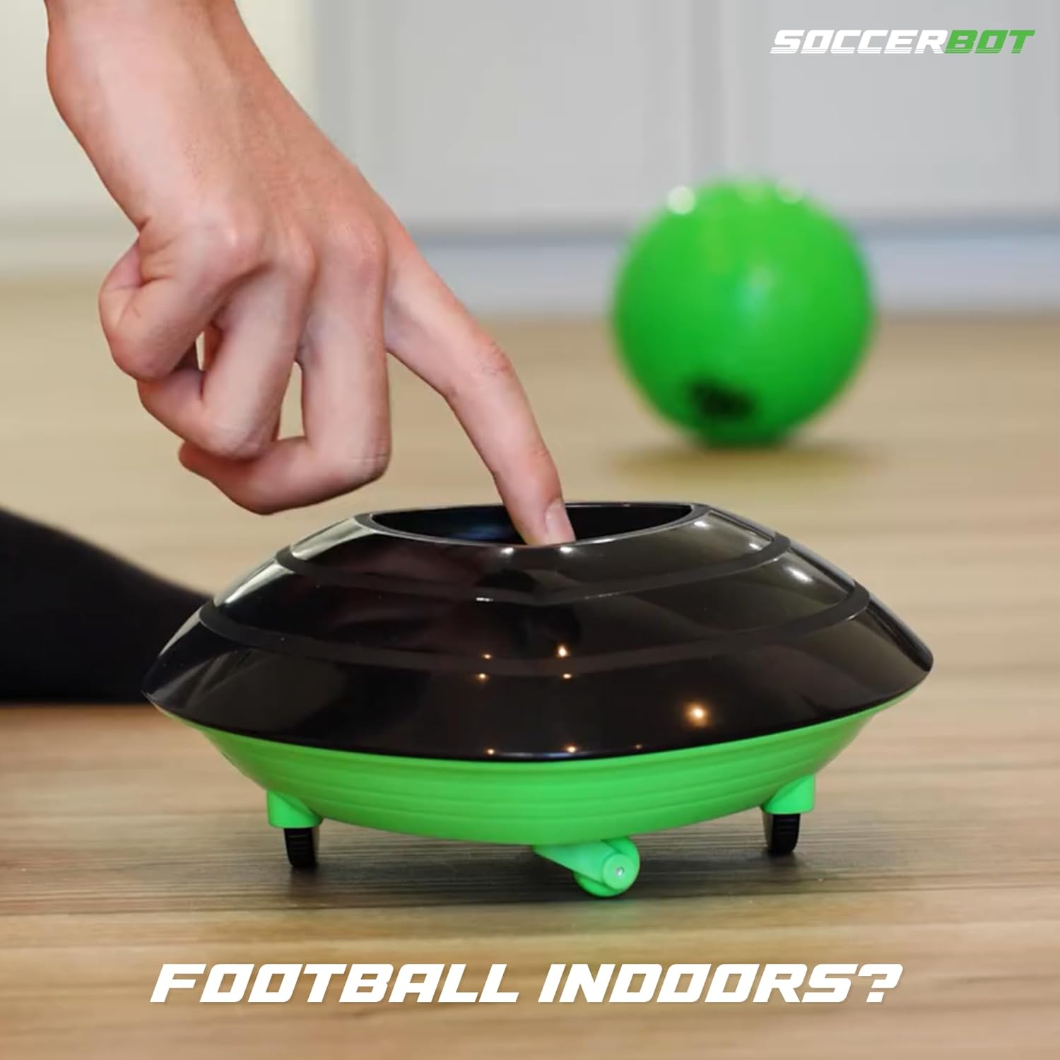 Green and black soccerbot toy on a wooden floor with a hand pressing a button.