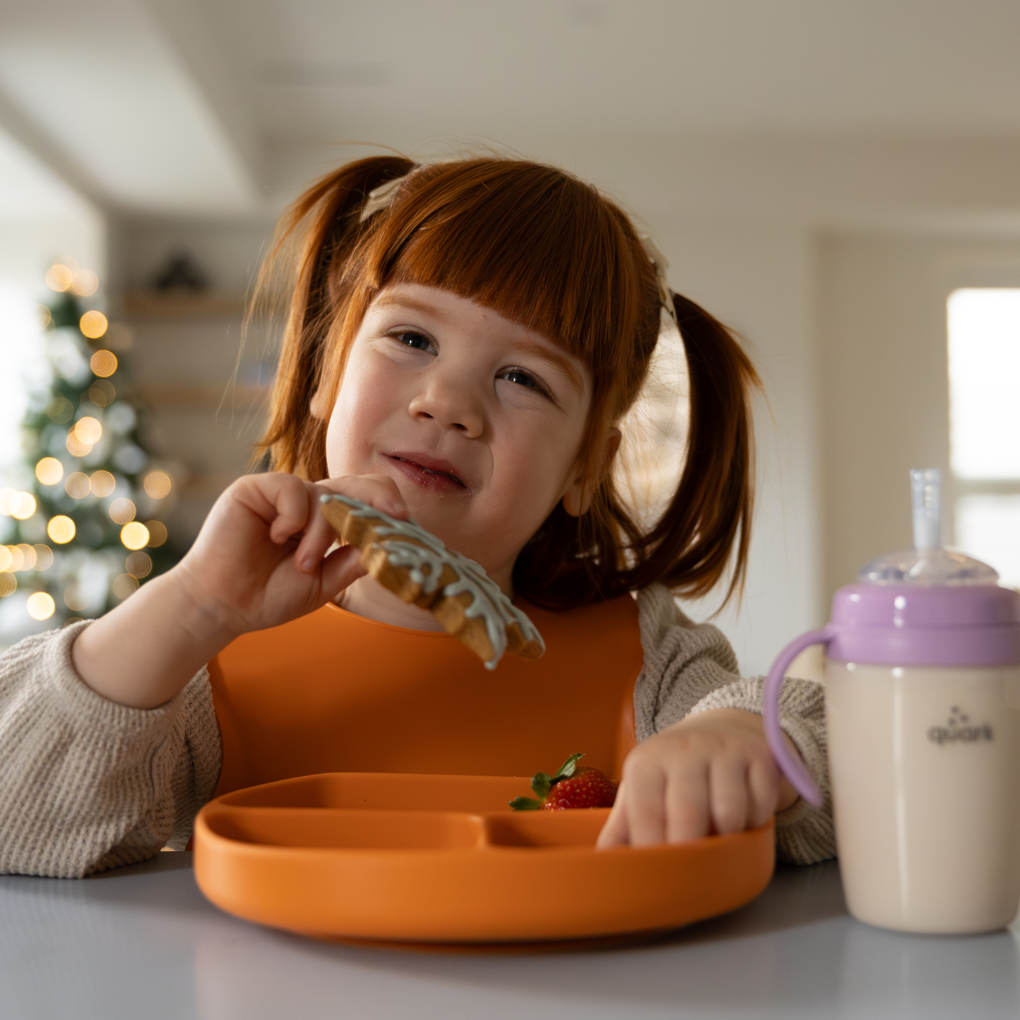 Child eating with an orange plate and sippy cup in a home setting