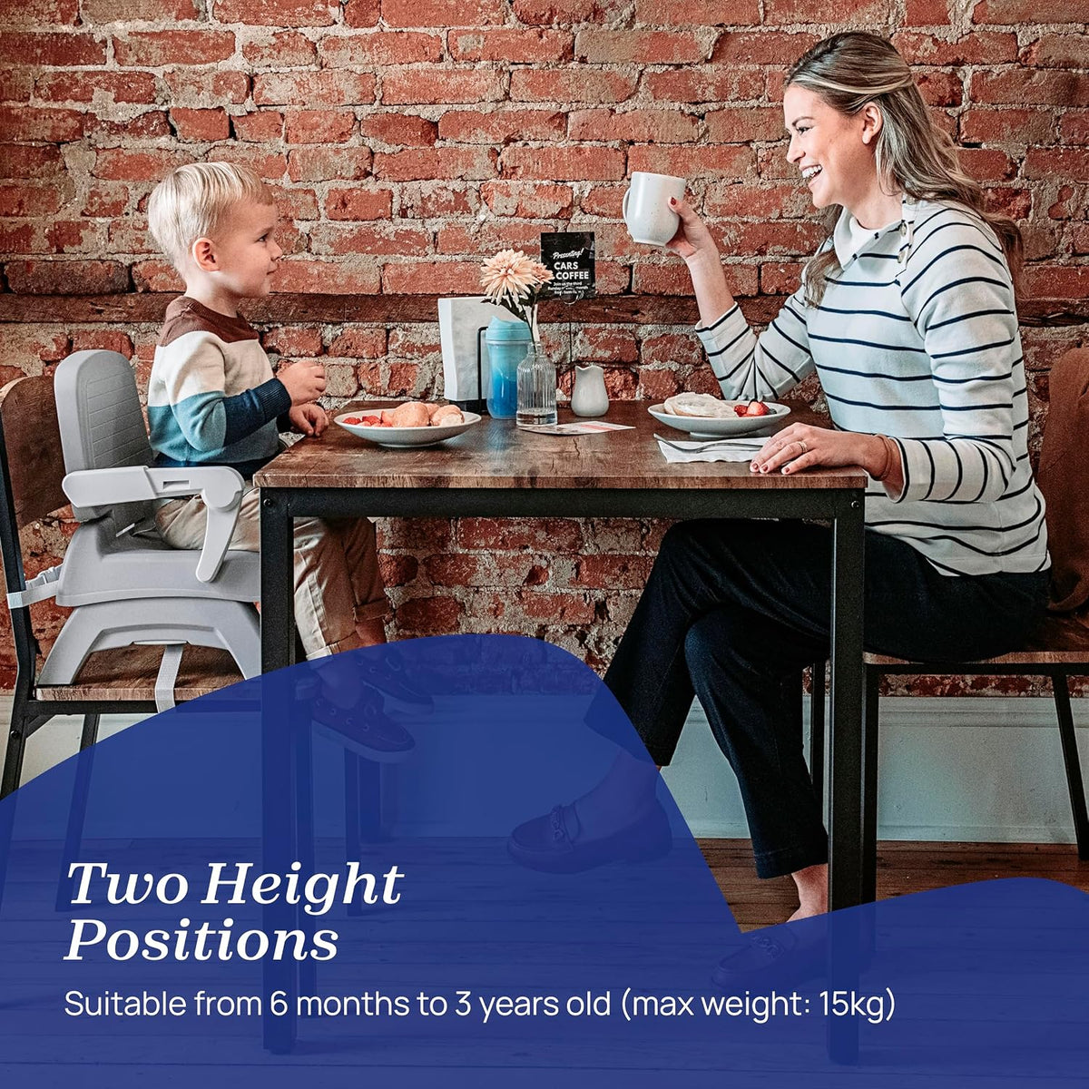 A woman and a young child sit at a wooden table in front of a brick wall, with the child using a high chair. A blue text overlay at the bottom reads 'Two Height Positions' and 'Suitable from 6 months to 3 years old (max weight: 15kg)'.