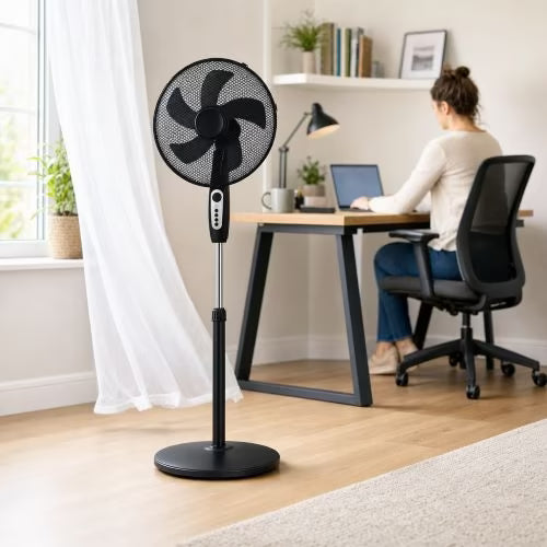 Crystal Home Air Comfort 40cm Pedestal Fan in Black - full view on a light wood floor in a bright home office, with a woman seated at a desk in the background.