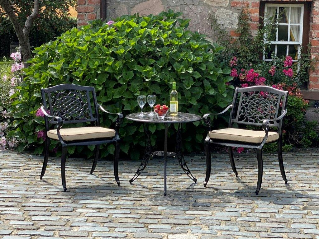 Outdoor patio set with two chairs and a table on a stone patio in front of a brick building.