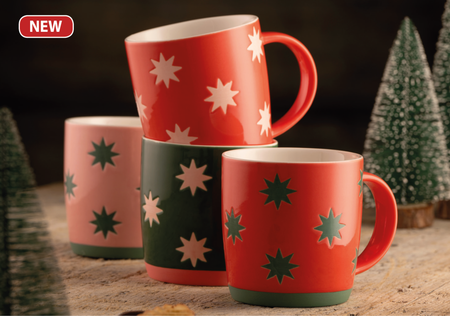 Set of red, green, and pink mugs with star patterns on a wooden surface.