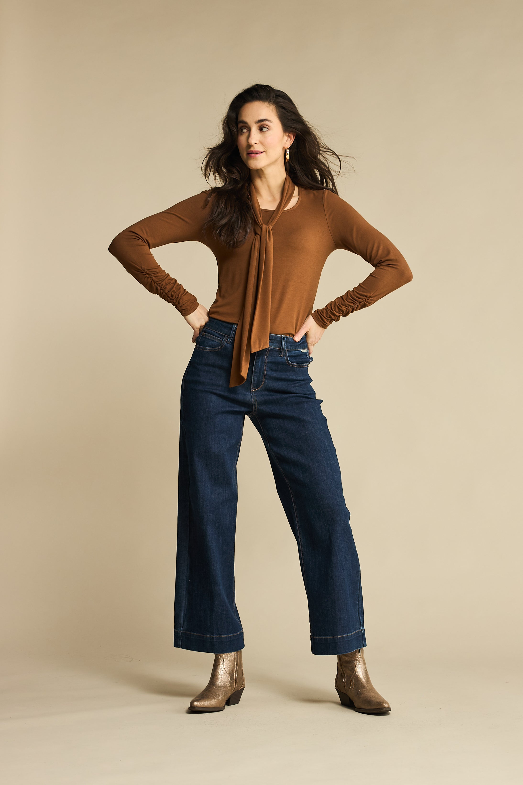 Woman wearing a brown top and blue jeans against a beige background