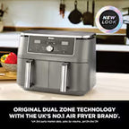 A countertop air fryer in dark gray and black with a stainless steel basket, shown in a kitchen setting. A circular badge says 'NEW LOOK' and text at the bottom reads 'ORIGINAL DUAL ZONE TECHNOLOGY WITH THE LEE'S NO.
