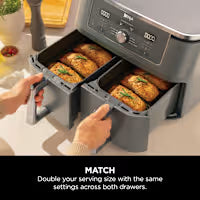 Ninja foodi multi-cooker with two drawers open, showing cooked food inside, on a kitchen counter.